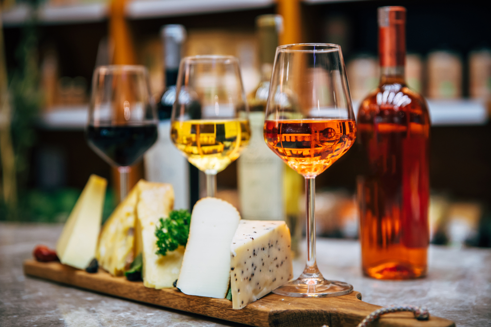 Plate of cheese sits with three different glasses of wine, pink white and red infront of wine bottles at a wineries in Fredericksburg