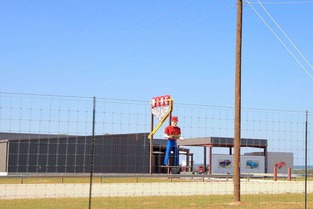 Large state of mechanic stands in front of a Wineries In Fredericksburg with a vintage sign reads Wine Garage