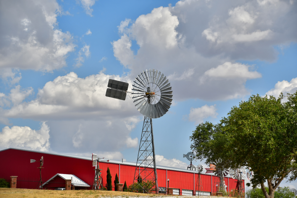 The exterior of one of the buildings at the Agriculture Museum. It is a long red building that looks like a warehouse and there are windmills around it.