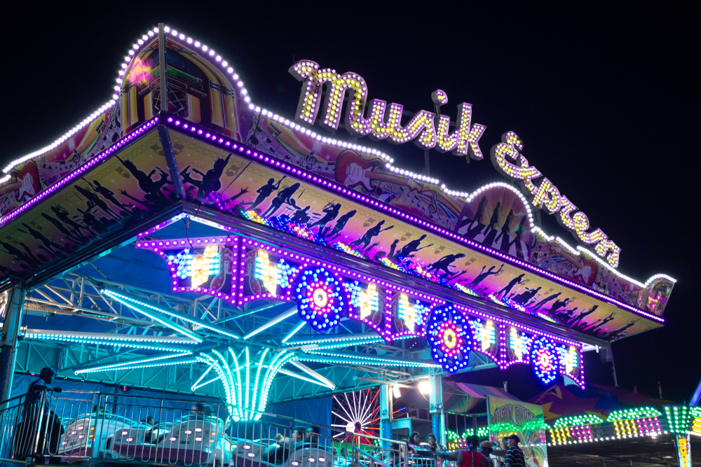 An amusement park ride lit up at night. It has blue, purple, and yellow lights. You can also see cars moving in it. Its one of the best things to do in Lubbock. 