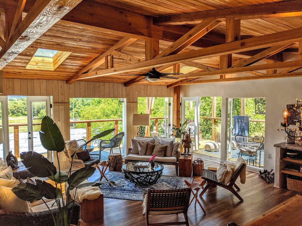 Living room of the Austin Luxury home shows two sets of double doors out onto a spacious deck. The home is furnished in an airy bohemian style. This is one of the best vacation rentals in Texas. 