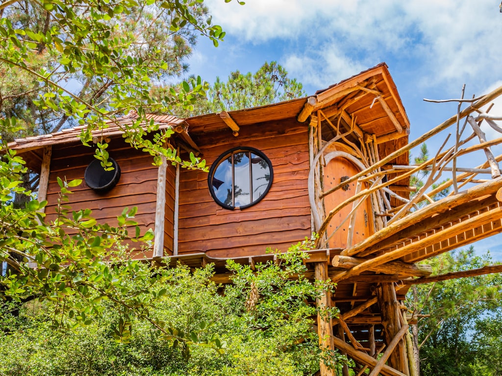 The exterior of the Hobbit's Nest Treehouse. There are round windows and a fantasy themed door knocker. This is definitely one of the best vacation rentals in Texas. 