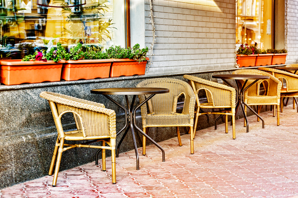 Sets of wicker chairs and patio tables in a brick courtyard for a bistro like you'd find at one of the best things to do in Wimberley. There are flower boxes in the windows and lights around them. 
