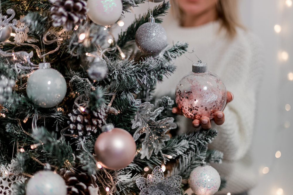 A woman places a decoration of a white ornament on a Christmas tree