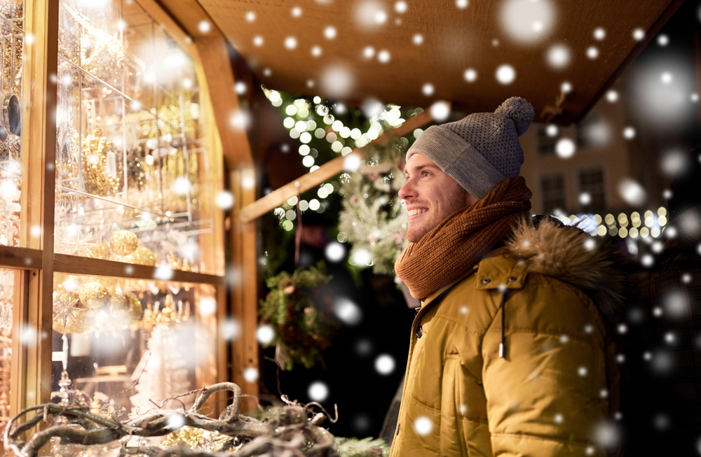 A man stares at a Christmas window shop while smiling.