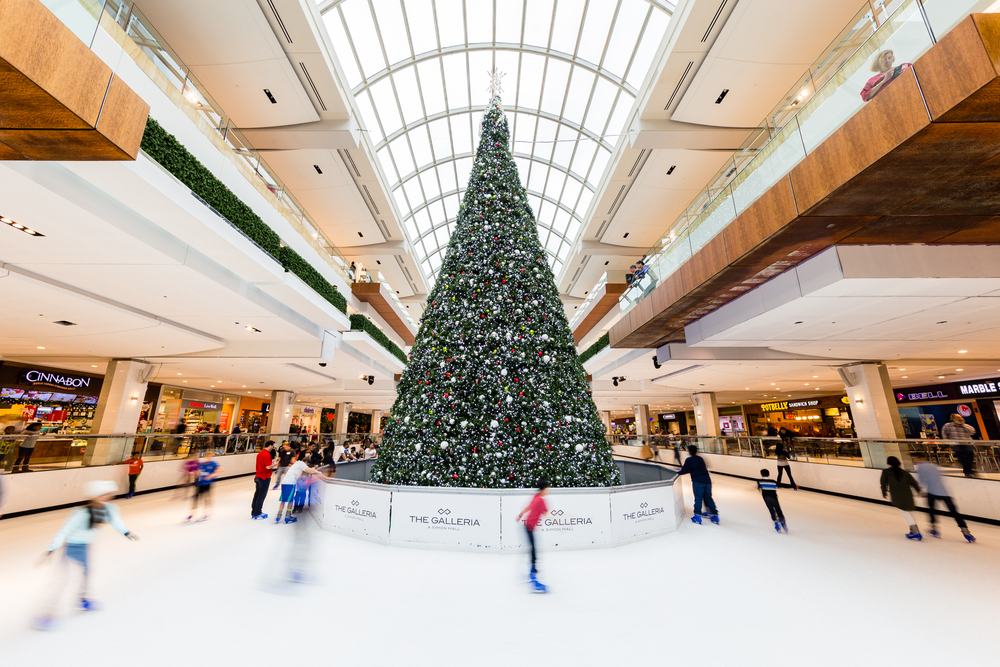 An indoor ice skating rink with a giant Christmas tree and skaters.