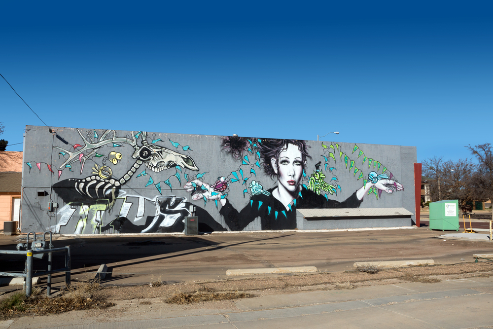 A mural of a woman, a deer skeleton, and vines on the side of a building in Lubbock Texas' historic Depot District. 