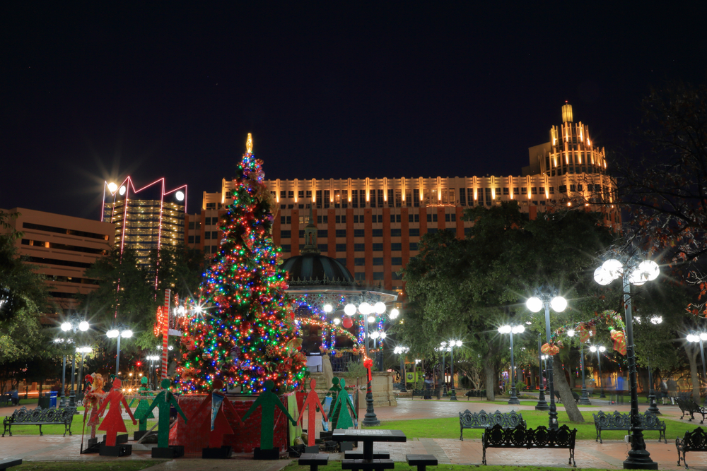 The historic market square in San Antonio. You can see a large historic building, palm trees, and a large Christmas tree covered in multi-colored lights. 