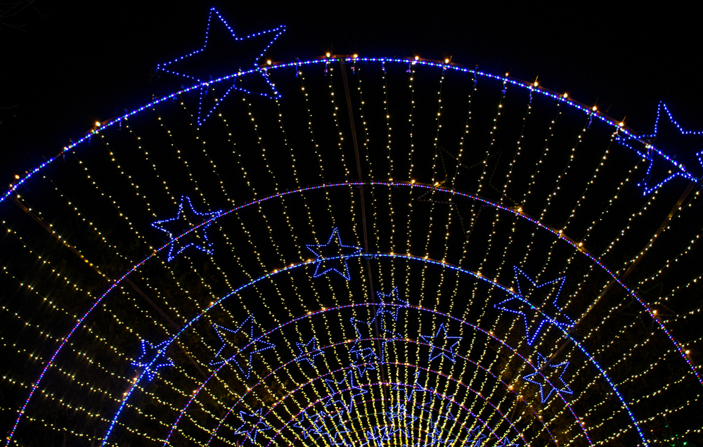 An archway of string Christmas lights with blue light up stars scattered throughout it. 