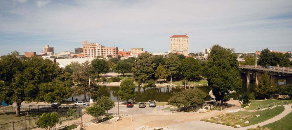 Looking past the river at the small skyline of Lubbock Texas. You can see lots of trees and a few tall buildings.