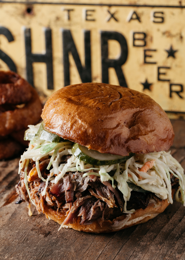 a bbq pork sandwich with coleslaw and pickles on a brioche bun