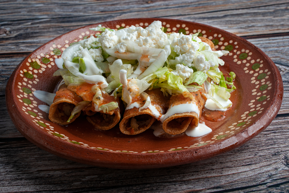 Flautas on a red plate with sour cream, lettuce and Mexican cheese