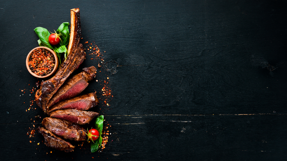 A bone in steak on a black serving trey with peppercorns