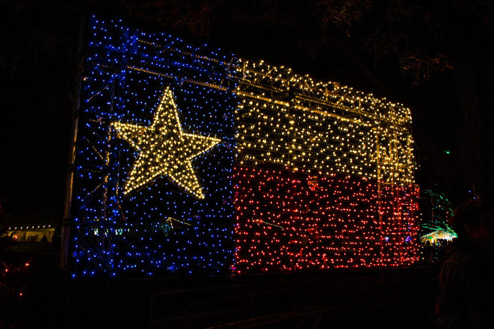 A large Texas state flag made entirely of colored lights in an area with other Christmas lights. 