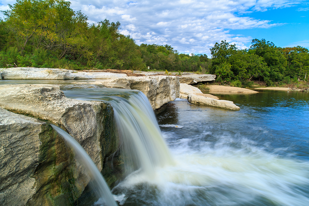 McKinney Falls a double waterfall flowing into water below on a sunny day