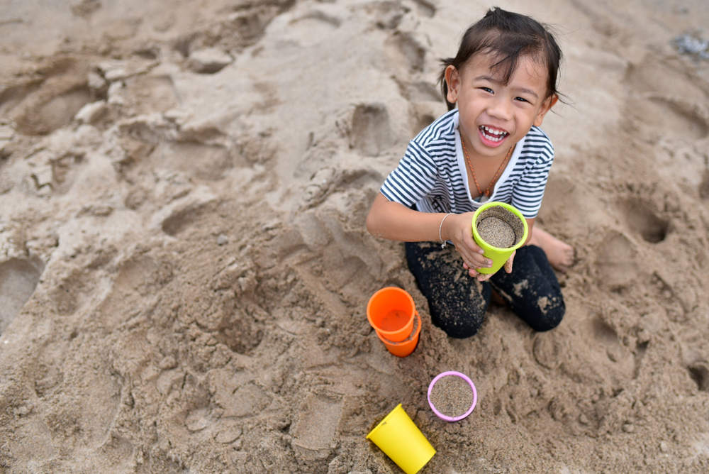 A child plays in the sand with colorful cups at Burger's Lake one of the most fun beaches near Dallas!