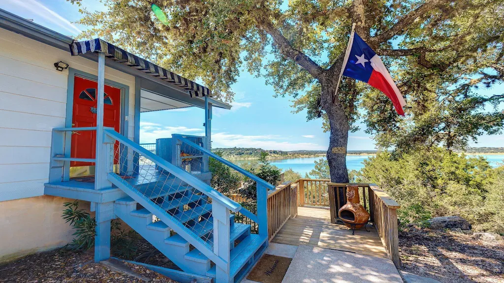 Sets lead to red front door of cabin with view of canyon lake in the background 