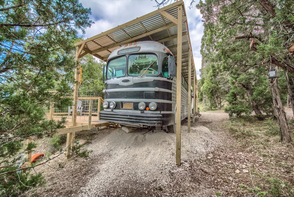 Old bus parked under a wooden structure with deck surrounded by trees 