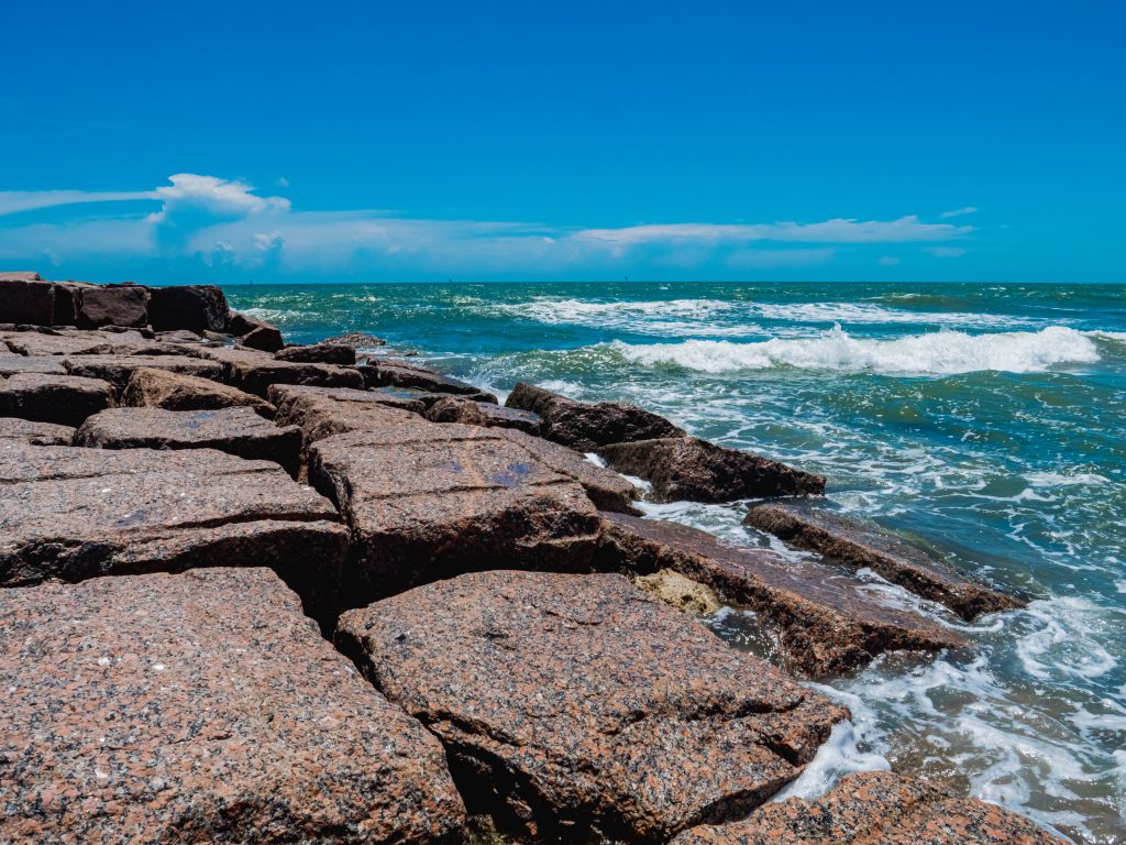 Large rocky coastline with bright blue waves crashing over the rocks  