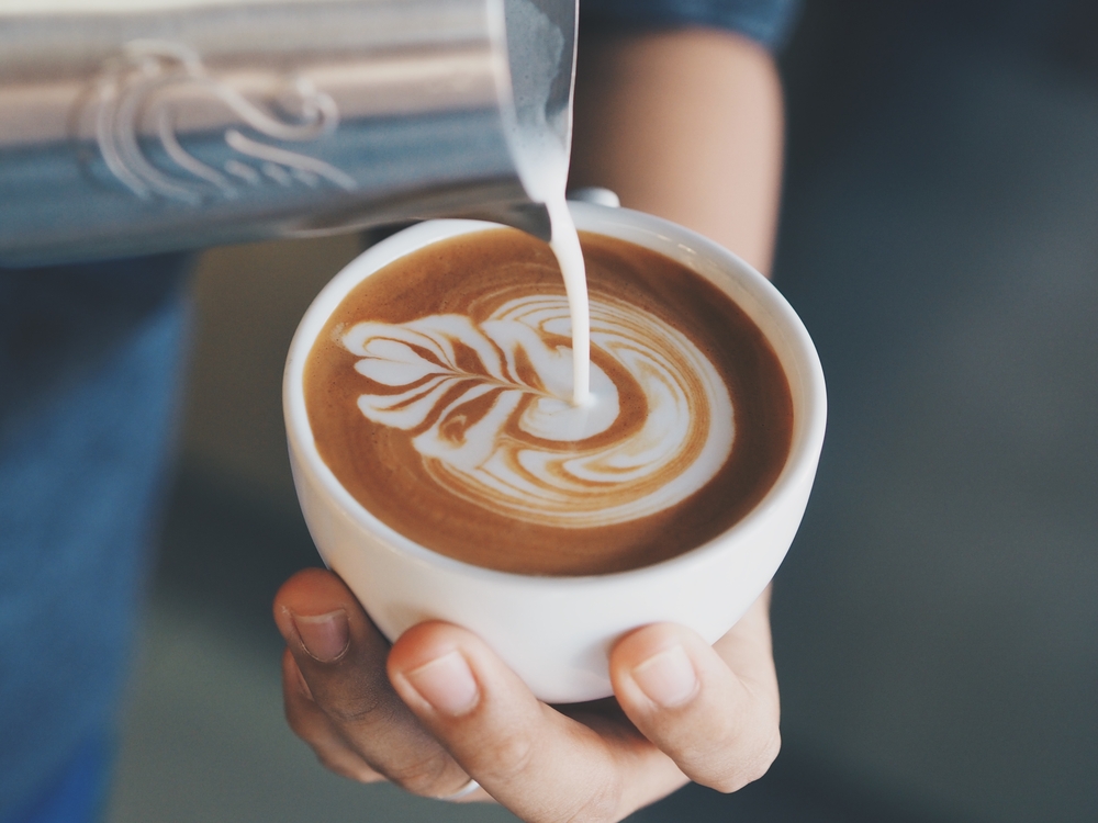 close up of baristas hands pouring steamed milk in latte creating a flower space in the cup
