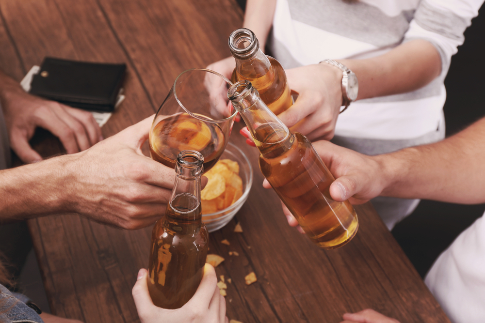 Two beer bottles and one glass being clinked together 