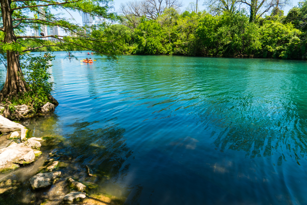 Blue water of Barton Springs, one of the best things to do in Austin, with kayakers in distance