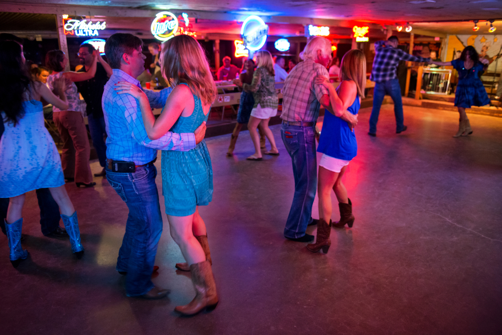 Couples country dancing with neon lights in background at Broken Spoke, one of the best things to do in Austin. 