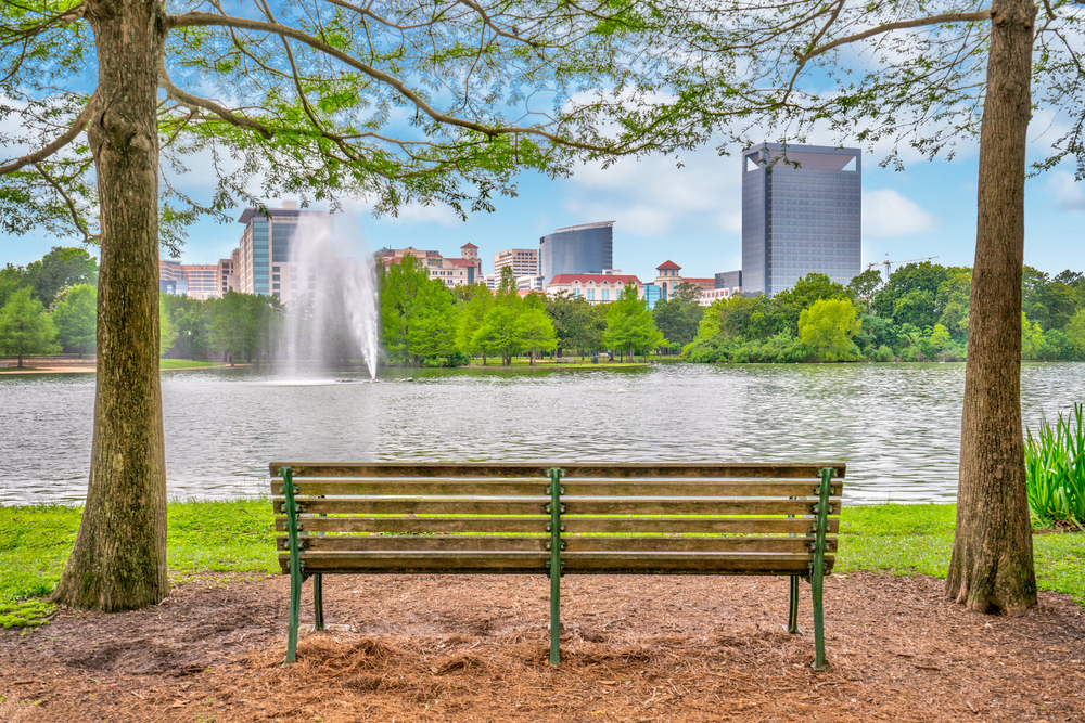 park bench on green grass with blue skies and fountain at McGovern lake, one of the best lakes in Houston