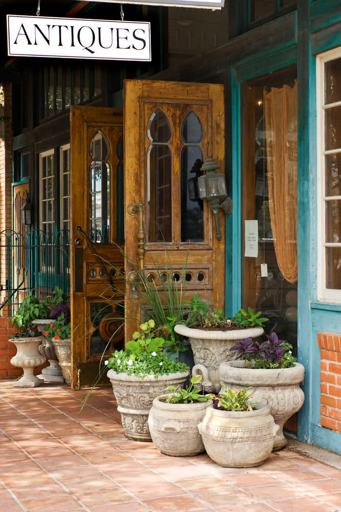 An antique shop on Main Street with wooden doors and potted plants on a brick sidewalk