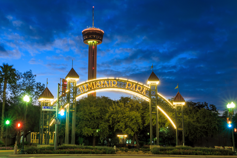 Night time sky over light up arch with text of Hemisfair Park, large tower and other things to do in San Antonio in the background