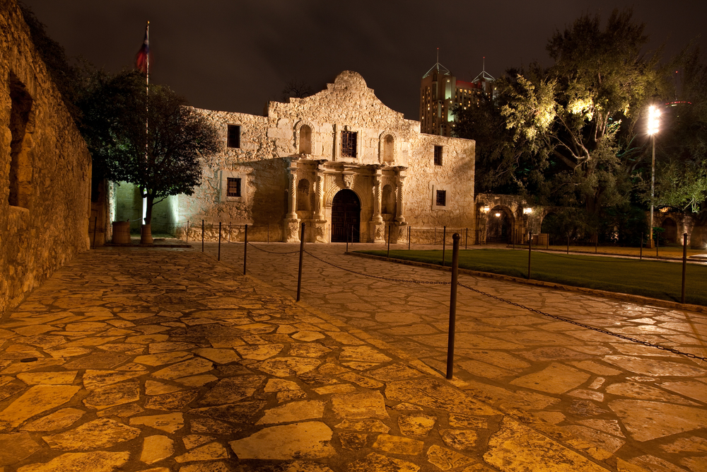 Nighttime shot of the alamo, stone front building with stone walkway in front and light post on left side