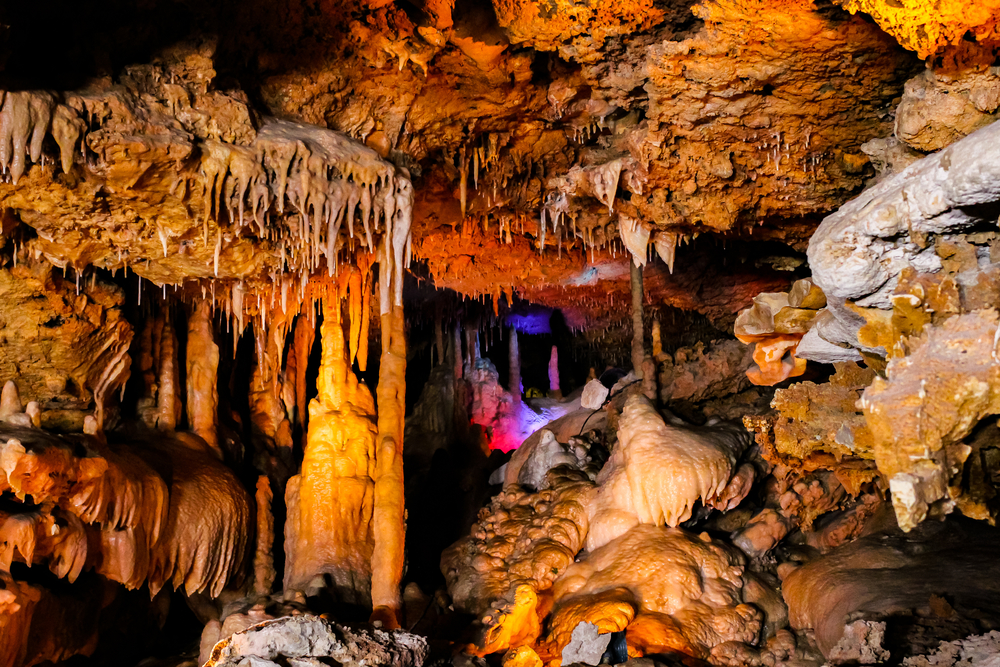 multiple cave formations through twisting spaces of cave with blue and pink light in center at Inner Space Cavern, caverns in Texas. 