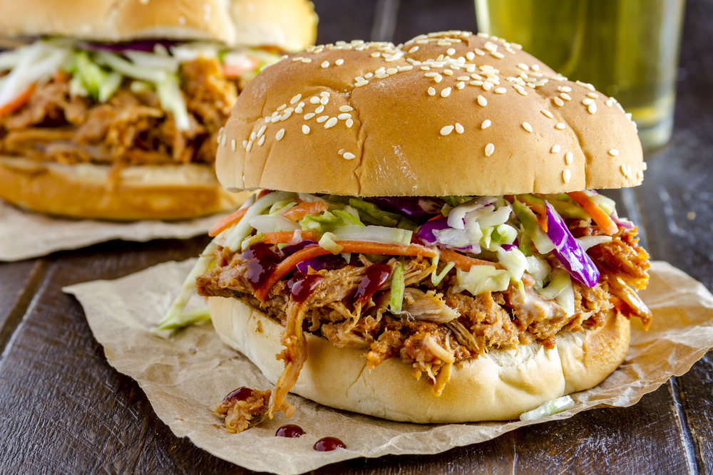 Pulled pork on a sesame bun with cole slaw and BBQ sauce on wooden table