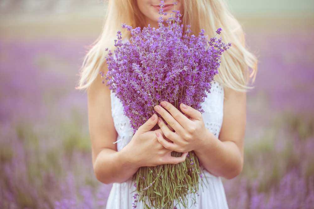 A blonde woman in a white dress holding a large bundle of lavender in front of her. 