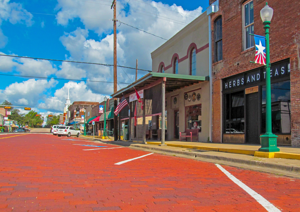 Red brick main street and city buildings against blue sky with clouds. In Mineola