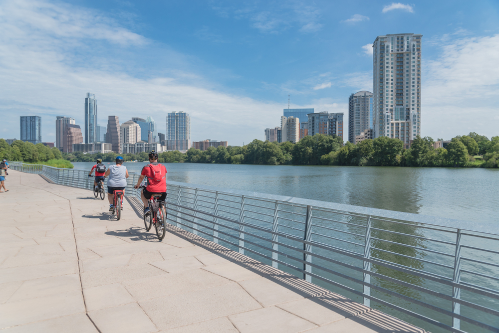 Couples and friends bike down the riverwalk on a tour, taking in the skyline of Austin: these biking tours are a fun way to have date night in Austin and explore the city through a new lens.