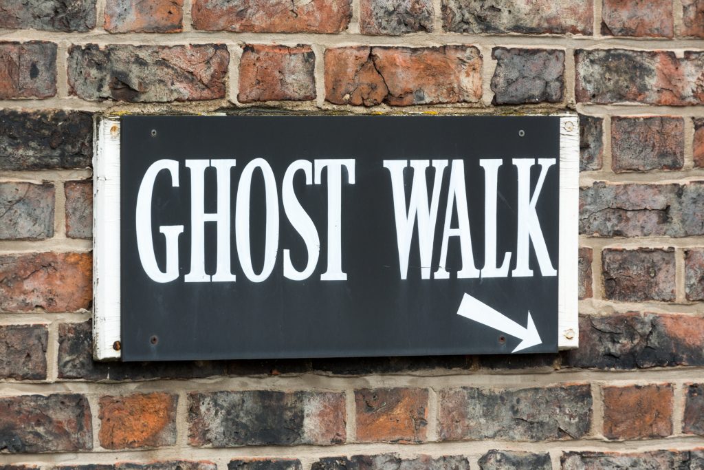 A sign that reads "Ghost Walk" signals tourists and locals where to meet for some spooky times: date night in Austin can be fun with adventures like the murder by gaslight ghost tour! 
