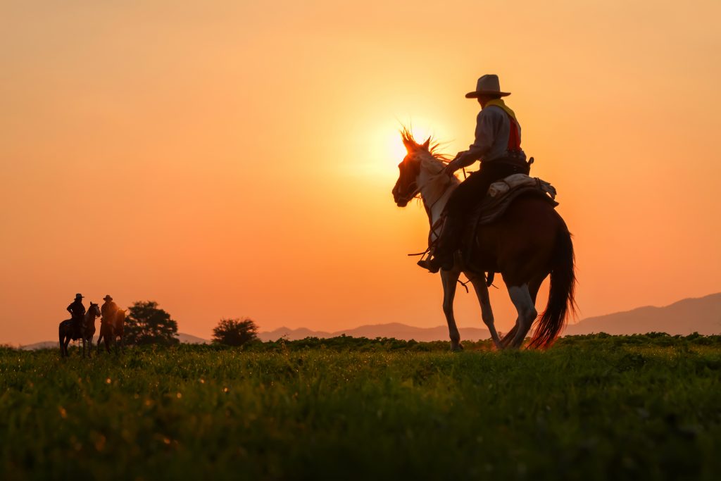 silhouette of three men wearing cowboy clothes riding on a horse texas dude ranches