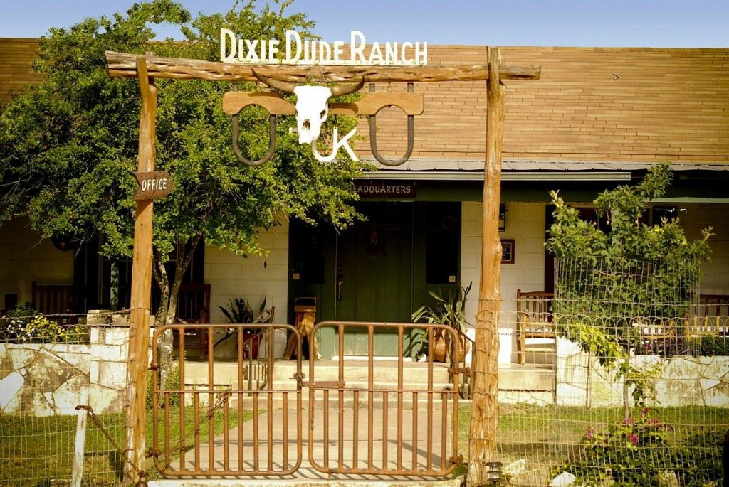 wooden gate with board of dixie dude ranch in front of a cottage-style building texas dude ranches