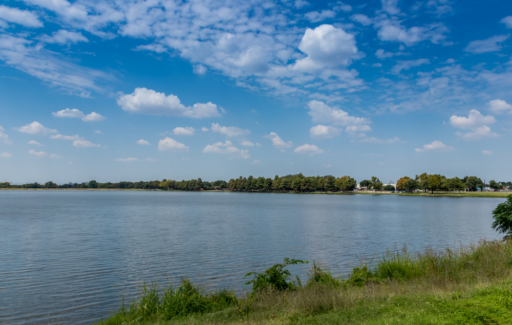 The blue of one of these lakes in Dallas contrasts the lighter blue sky, clouds, and green surroundings. 