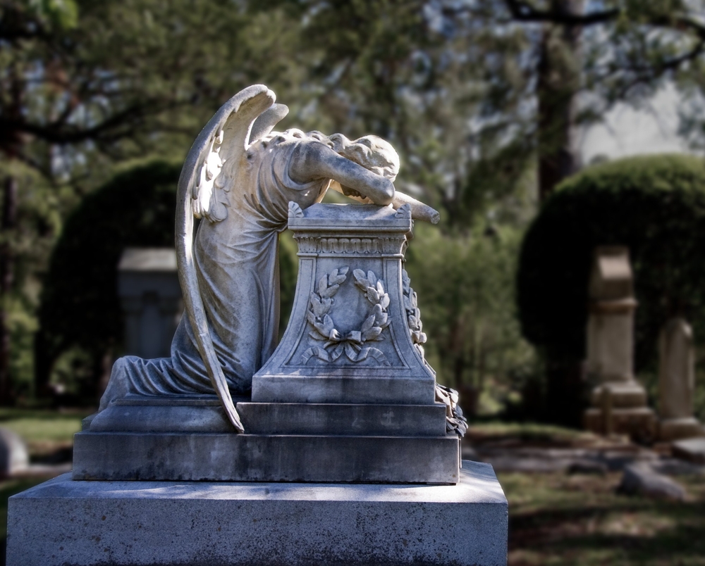 A weeping angel statue in a cemetery on a sunny day