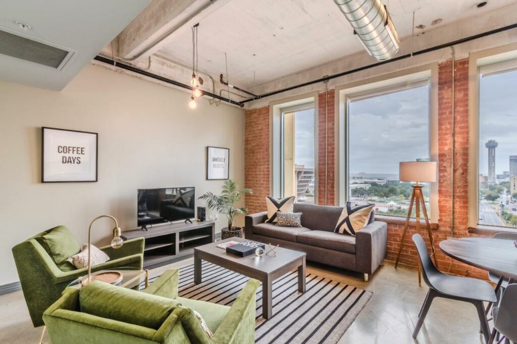 This apartment features high ceilings and massive windows that look out over downtown. The green armchairs are inviting you to sit, relax and look, almost as if they want this to be the place of where to stay in Dallas. 