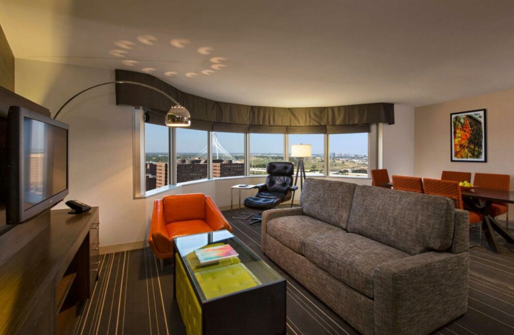 A couch faces a TV with modern decoration and a huge window that looks out over downtown in this hotel. It is one of the many places of where to stay in Dallas. 