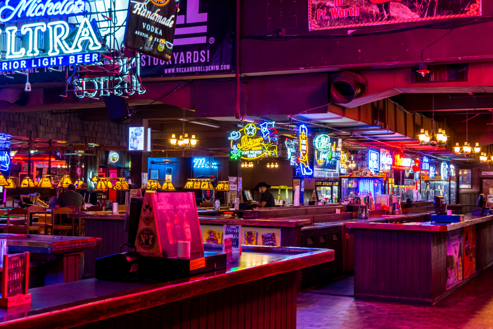 A bar in the Knox-Henderson area shows that this is where to stay in Dallas for nightlife: the pink and blue hues of the neon lights flash the area In colors as people work at the bar.