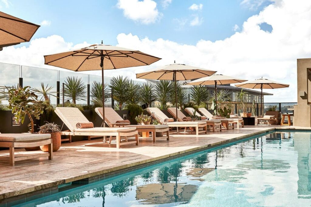 The Austin Proper Hotel is where to stay in Austin: the long pool has blue water and chairs with comfortable umbrellas on the patio. 