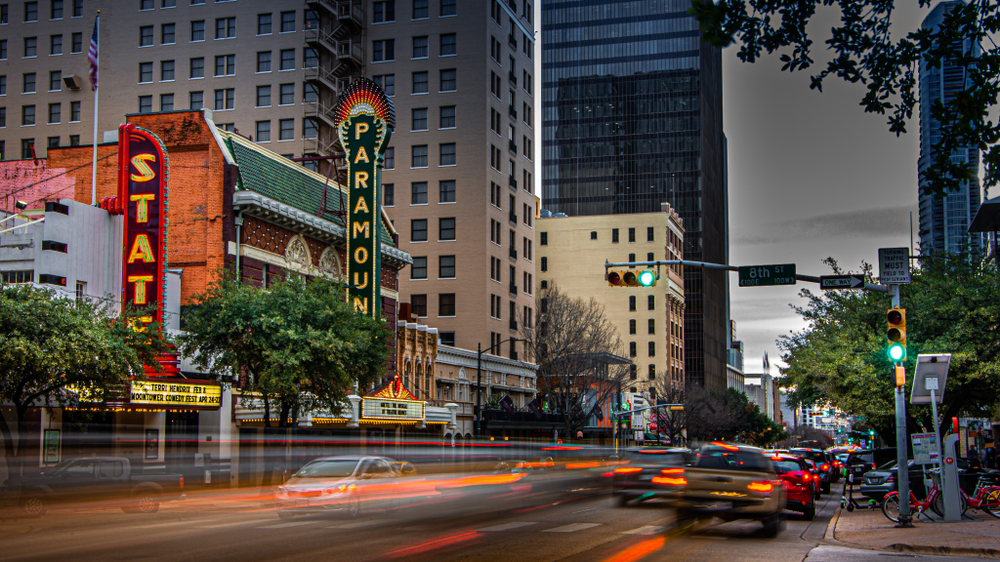 Cars zoom by in the evening while downtown Austin-- which is where to stay in Austin-- begins to turn on all its neon, night lights. 