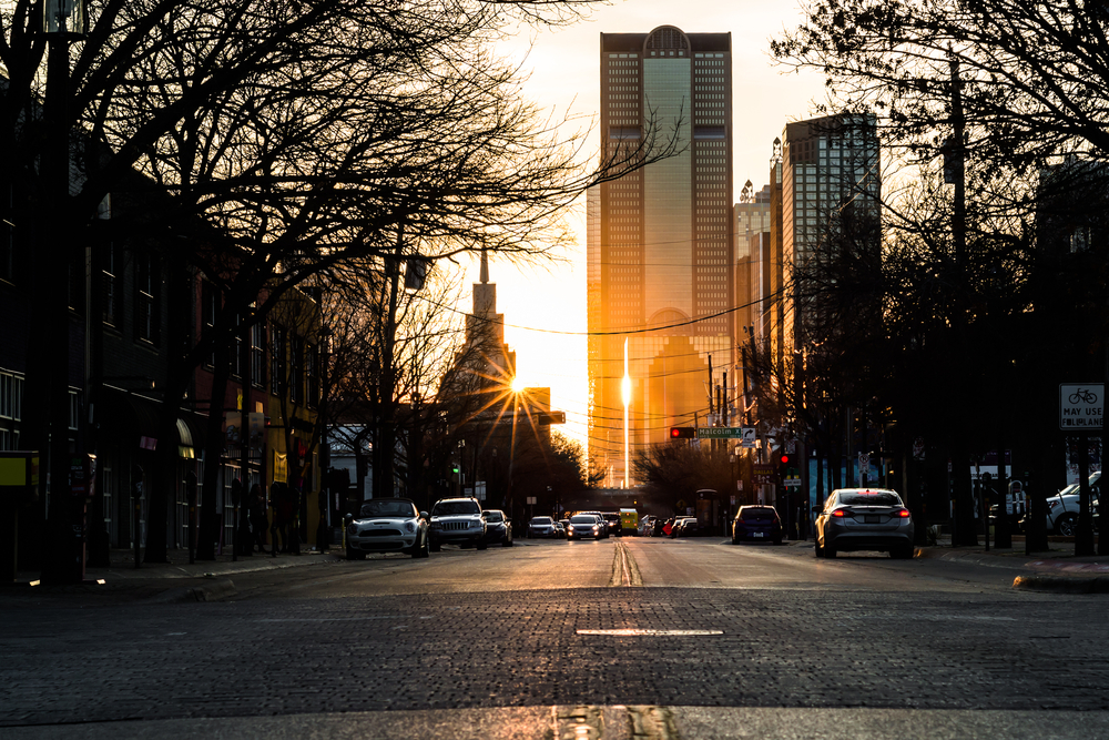 Downtown Dallas at sunset shows a street with skyscrapers, cars lining streets and more. Downtown is where to stay in Dallas for first time visitors. 