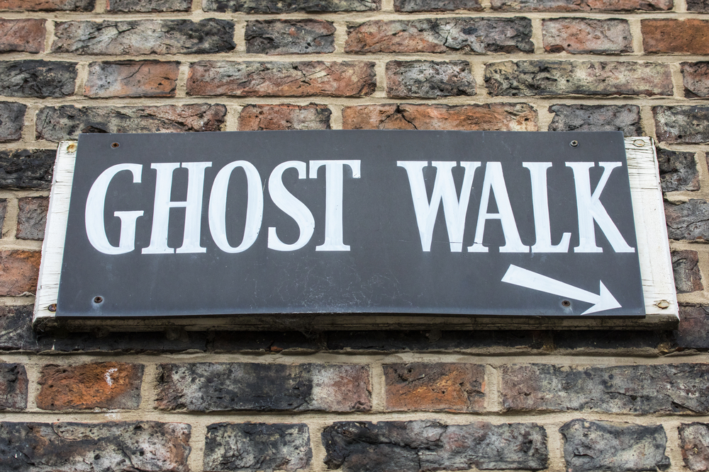 A sign that hangs on a brick wall advertises "ghost walk" in bold, white letters. Ghost tours are always one of the best things to do in Houston at night.