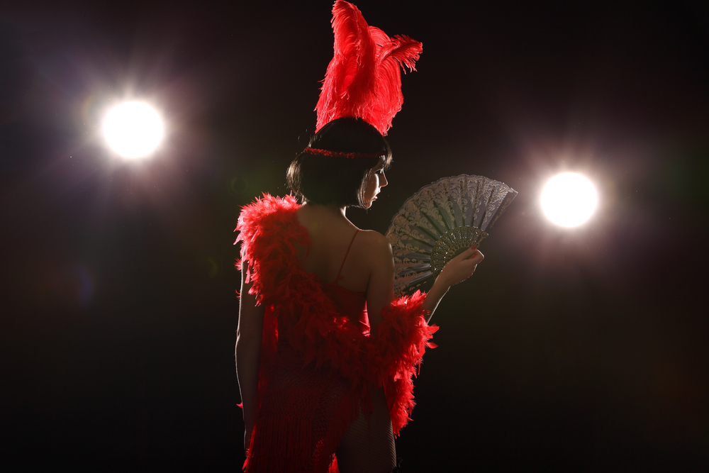 A woman in a burlesque costume that is composed of red feathers looks off toward the dark stage. Burlesque shows and live entertainment are some of the best things to do in Houston at night! 