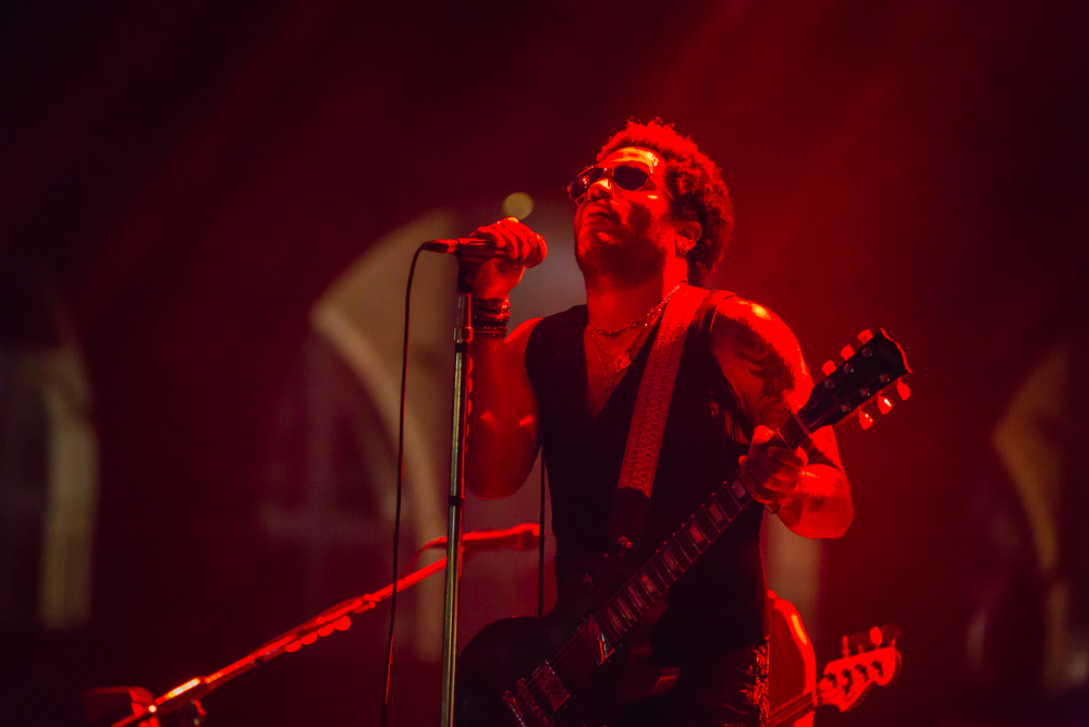 Of all of the best things to do in Houston at night, live music is also popular! In this photo, Lenny Kravitz preforms. He is bathed in a sea of red light and clutches a mic and his guitar. 